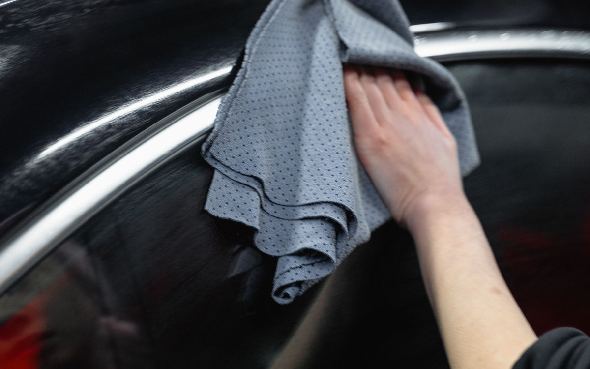 Hand drying a black car with a grey microfibre towel (real photo, Pexels / Tima Miroshnichenko)